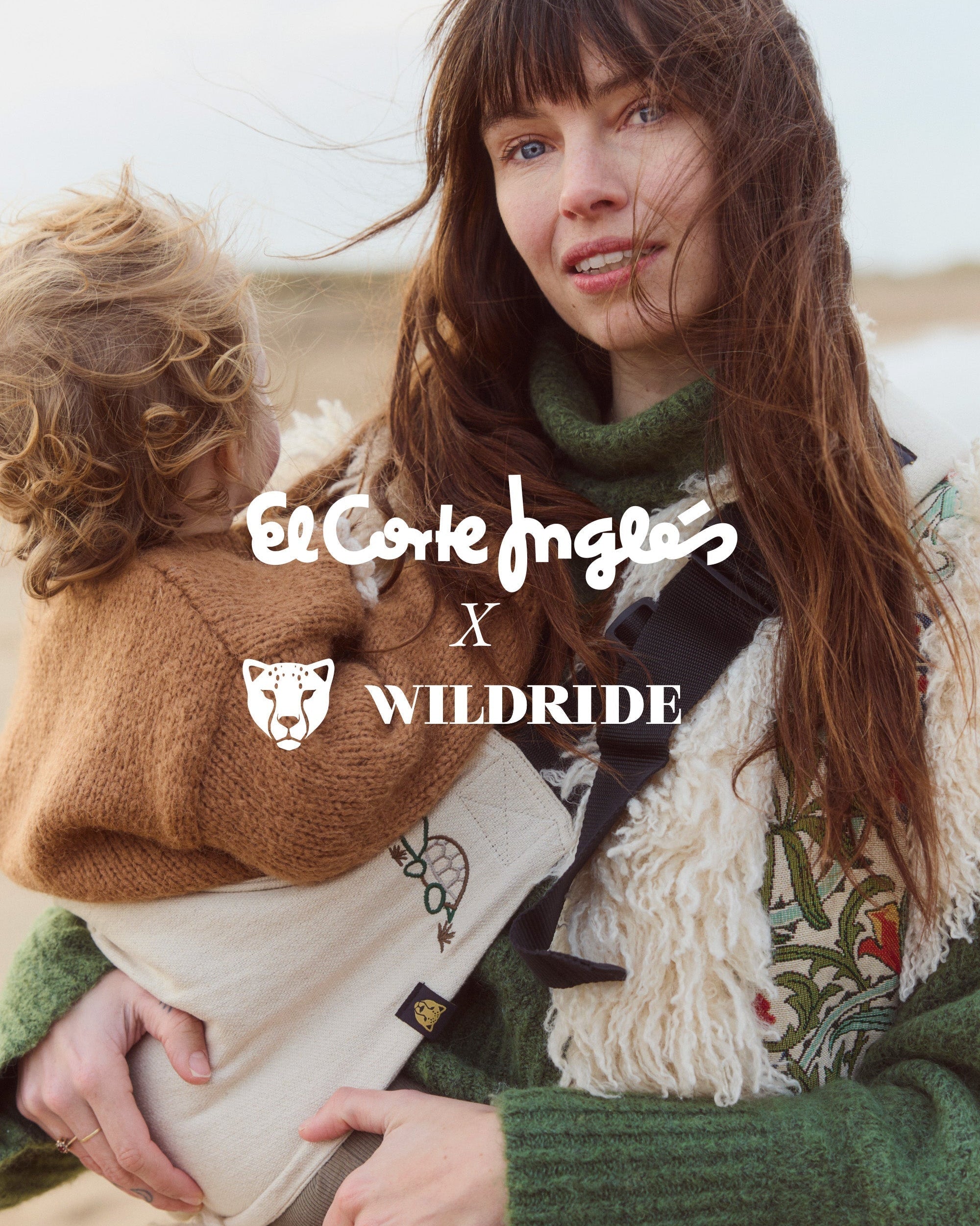 A close-up of a mother holding her toddler in the exclusive Wildride toddler carrier with turtle embroidery, created in collaboration with El Corte Inglés. The image features both brand logos in the center.