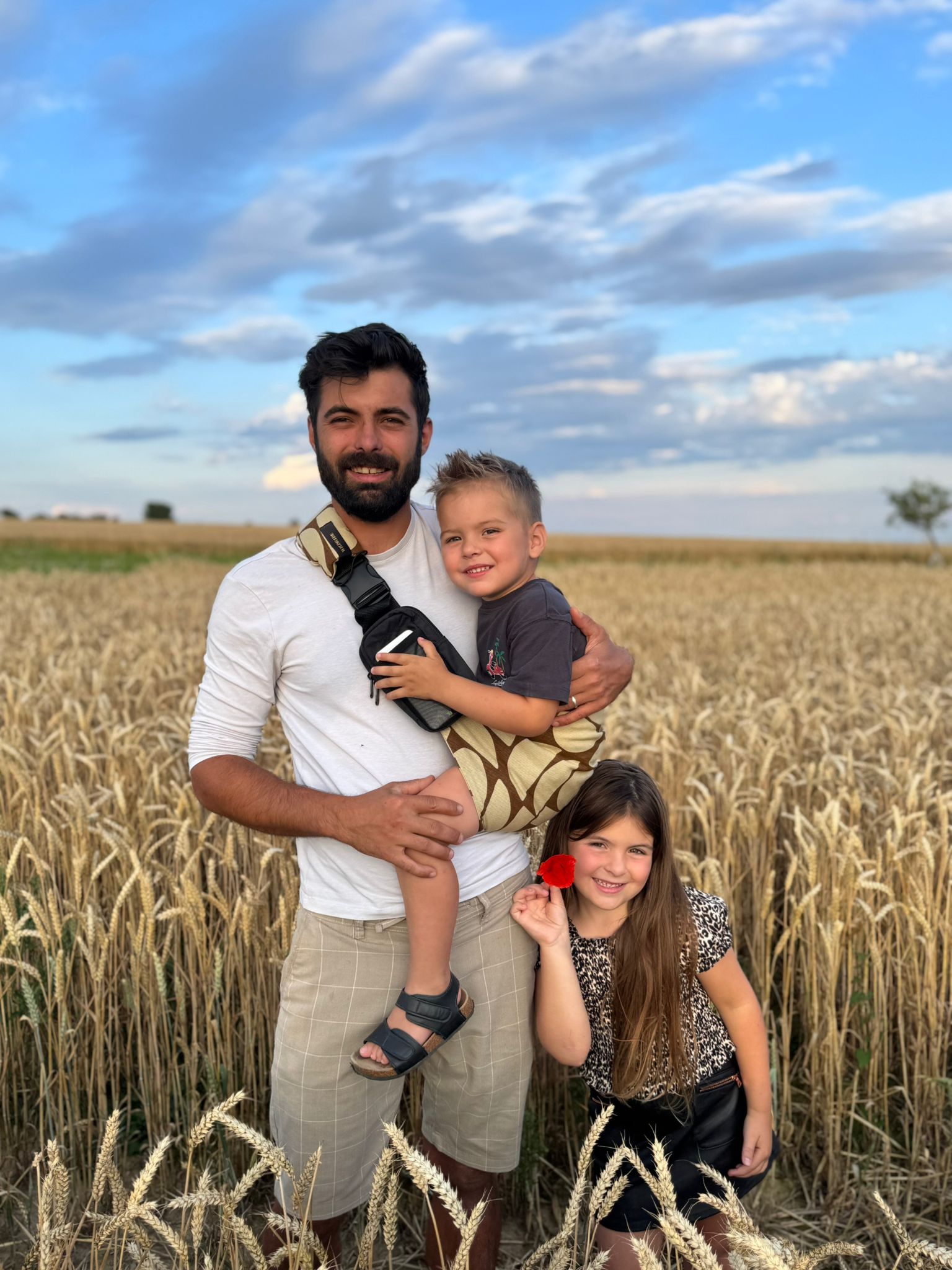 Father carrying toddler in Wildride baby carrier with daughter standing in wheat field