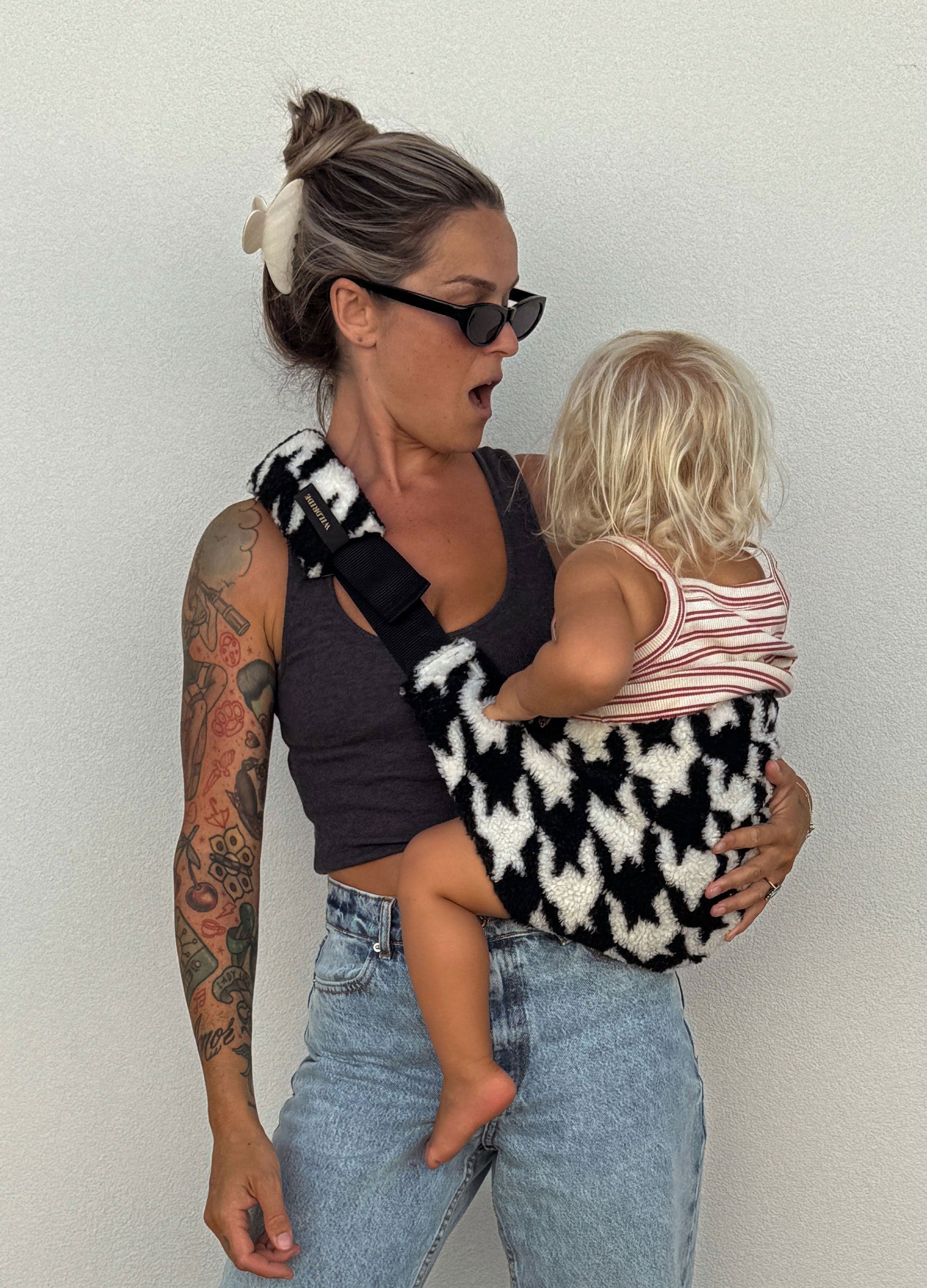 wildride houndstooth teddy toddler carrier — mom carrying child on hip against white wall