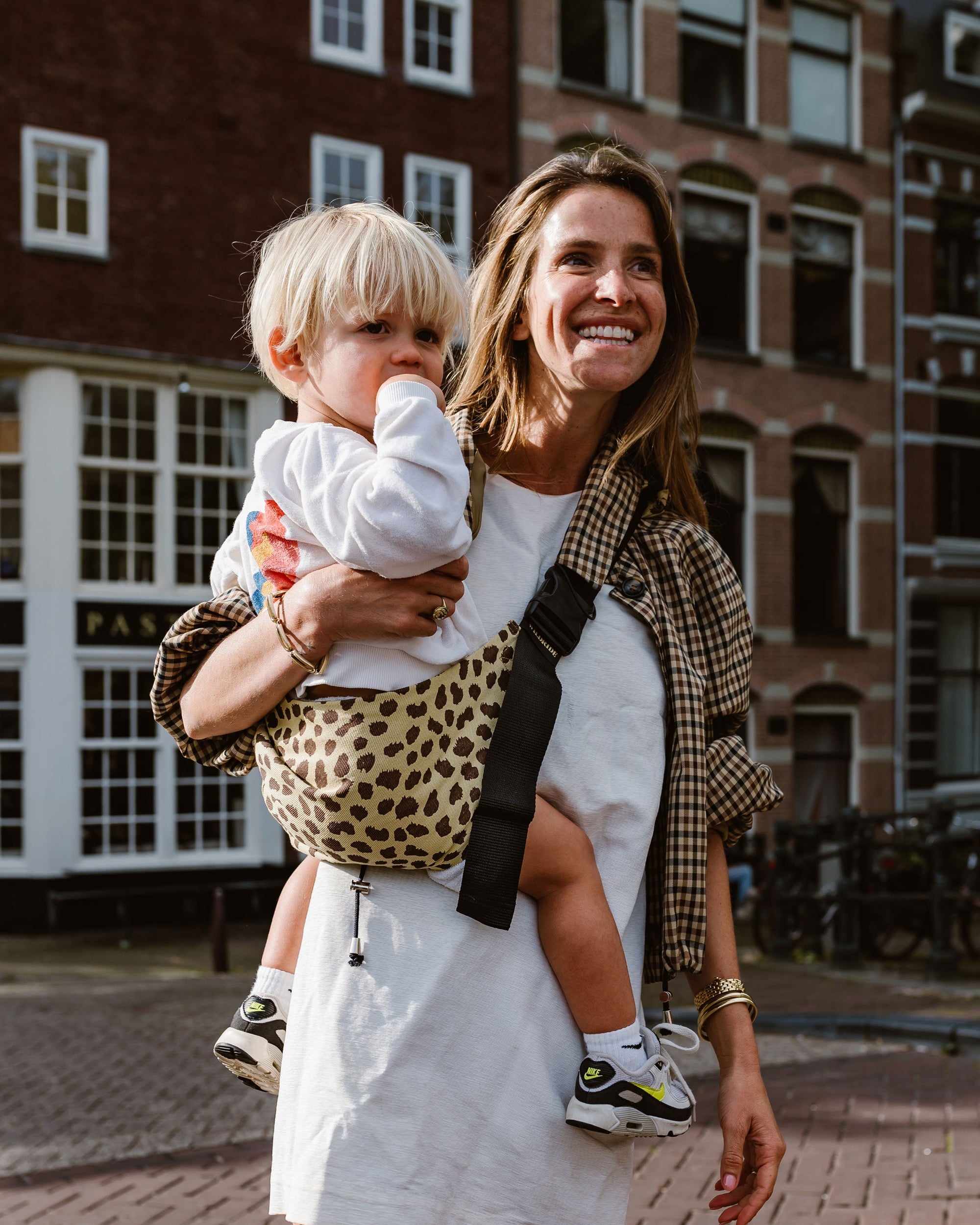 Wildride toddler carrier cheetah print, mom walking with child on hip on a city street