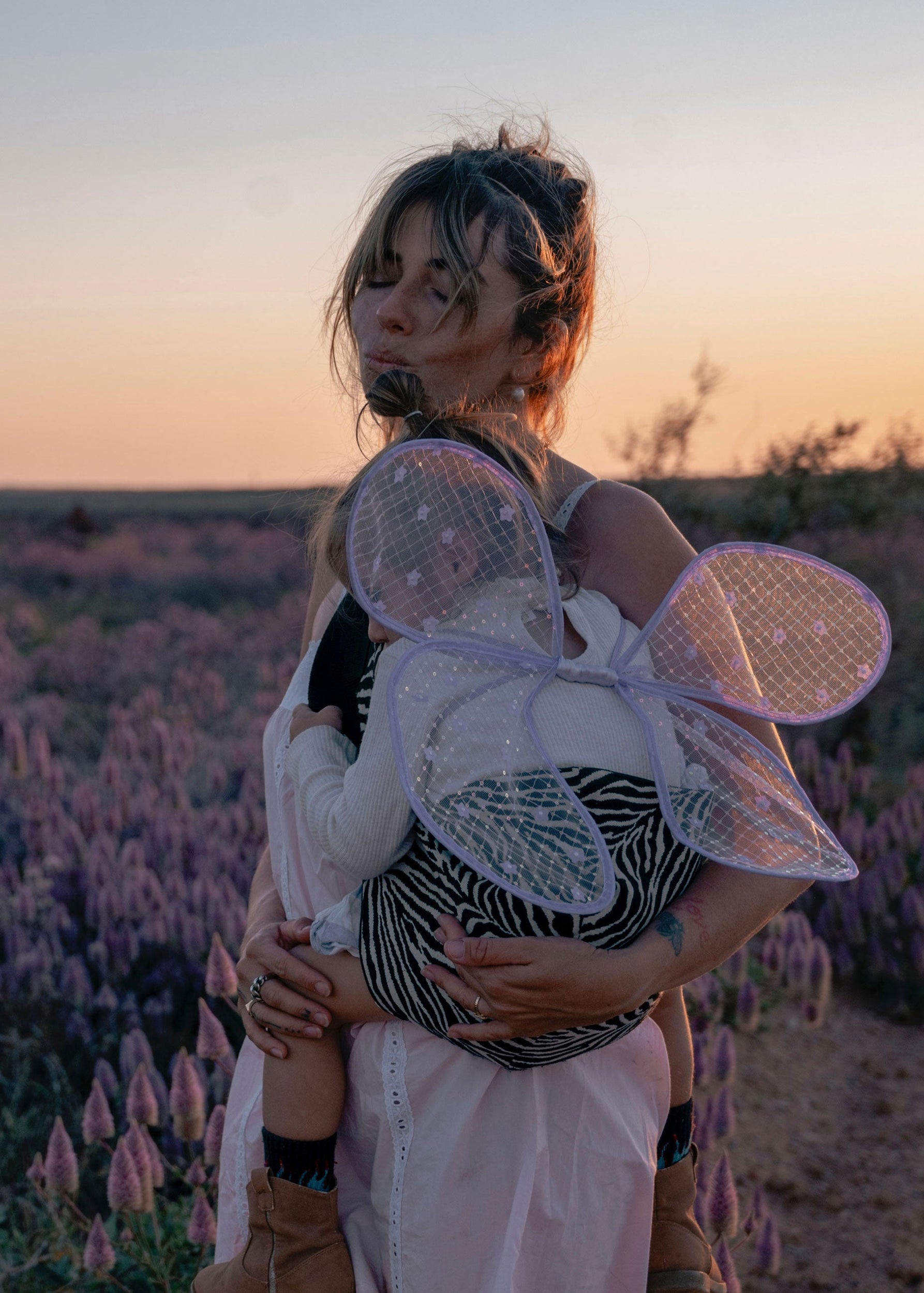 Wildride toddler carrier worn by mother carrying her child in a flower field at sunset